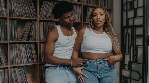 A couple in jeans and white shirts sitting in front of a record shelf