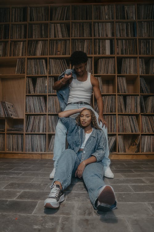 A couple sitting on the floor in front of a record shelf