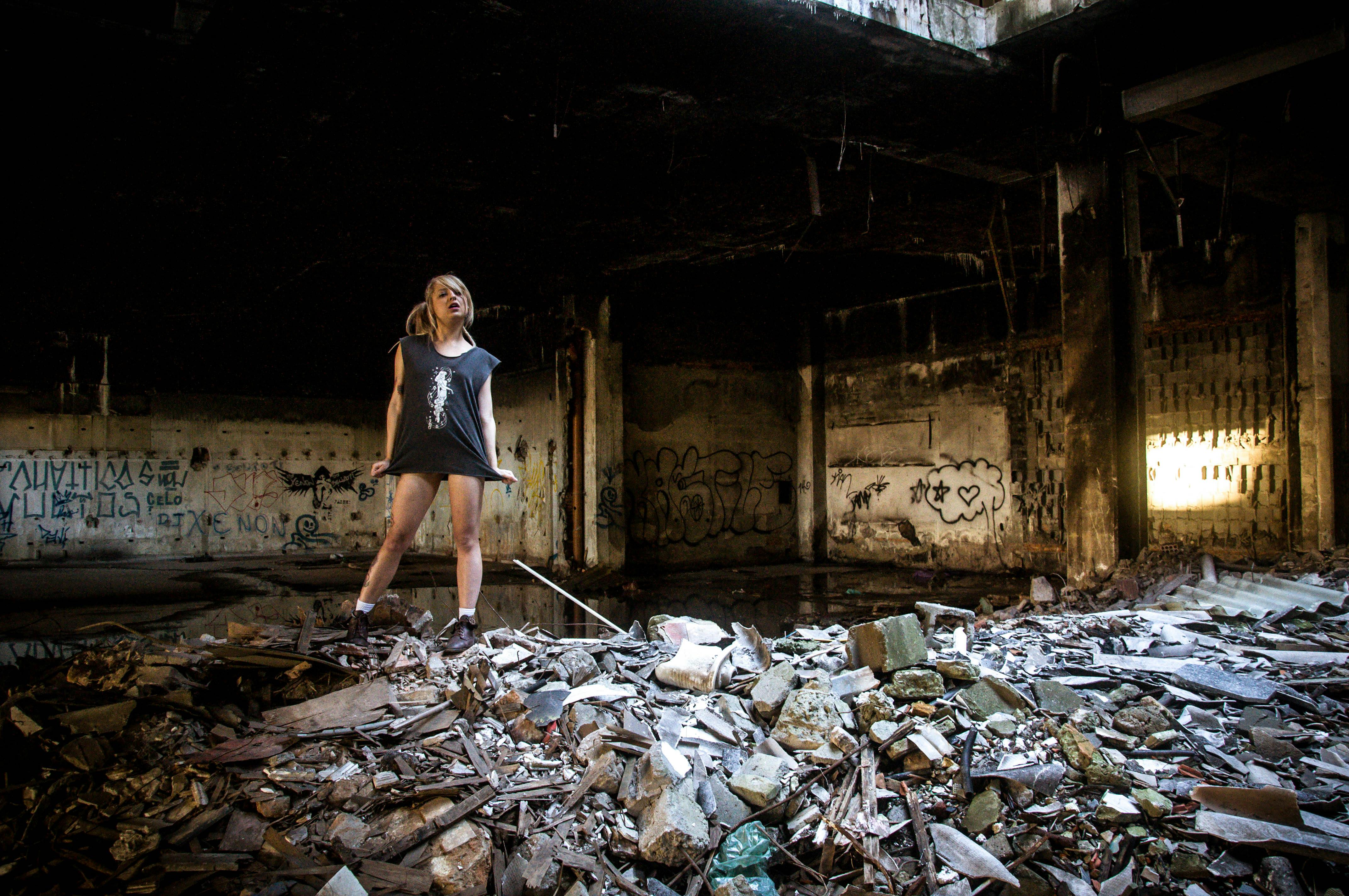 A tattooed woman in an abandoned building surrounded by debris and graffiti.