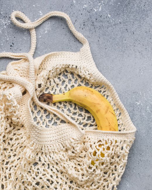 Eco-friendly reusable knitted bag with a fresh banana on concrete surface.