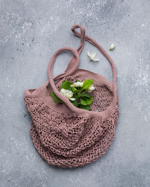 Sustainable crochet bag with green leaves and white blossoms on a textured surface.