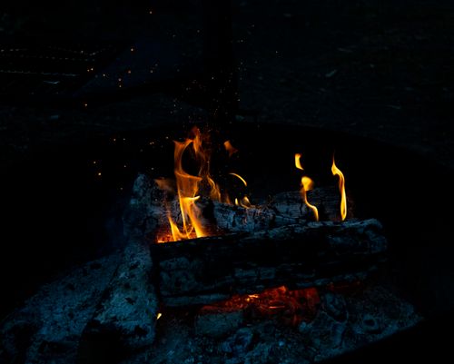 Free A campfire with glowing flames and embers in a dark outdoor setting, creating a rustic ambiance. Stock Photo