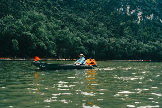 Serene river scene with a boatman in a conical hat, Ninh Binh, Vietnam.