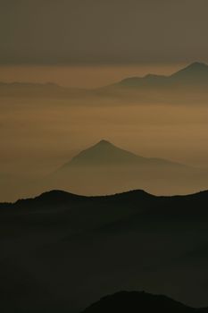 Serene view of mist-covered mountain peaks at dusk, enveloped in calming fog and clouds.