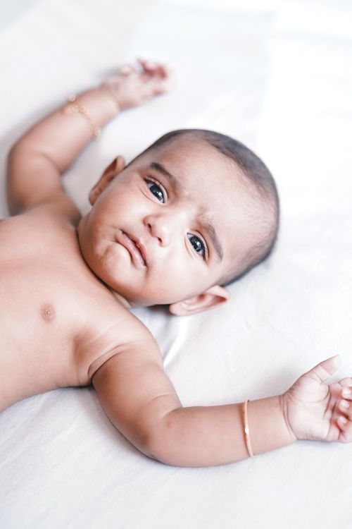 Free Cute baby lying on a white sheet with arms raised and a curious expression. Ideal for family and childhood themes. Stock Photo