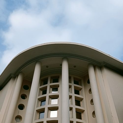 Free Elegant modern facade with circular windows and columns under a cloudy sky. Stock Photo