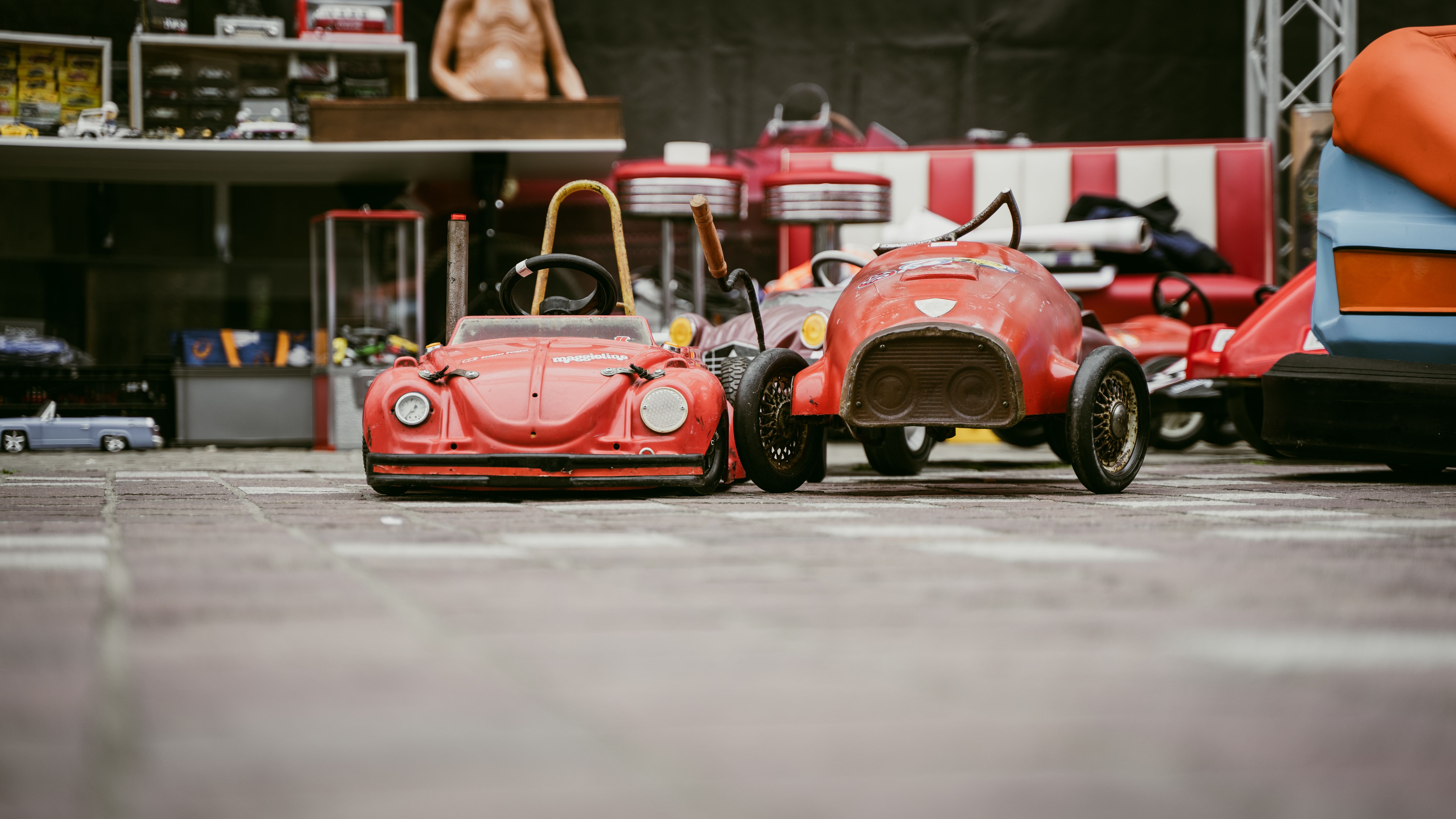 Close-up of vintage red toy cars displayed in an urban entertainment setting. Selective focus and nostalgic vibe.