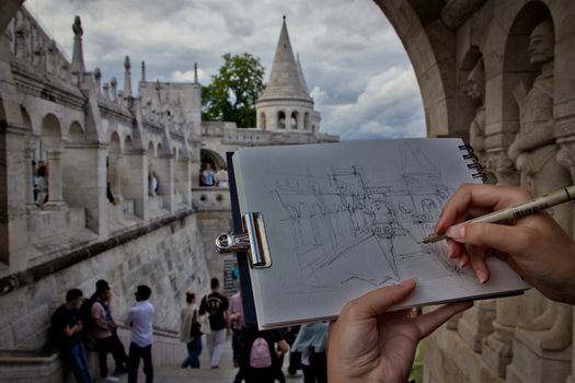 A person sketching the iconic Fisherman's Bastion in Budapest with people in the background.