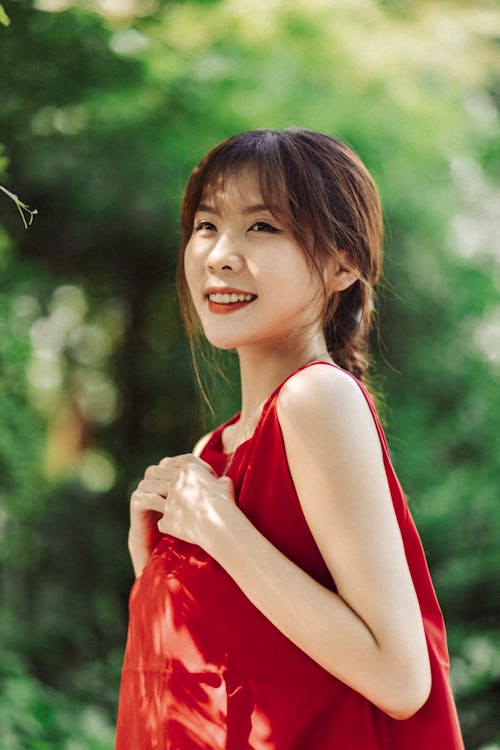 A woman in a red dress smiling in the woods