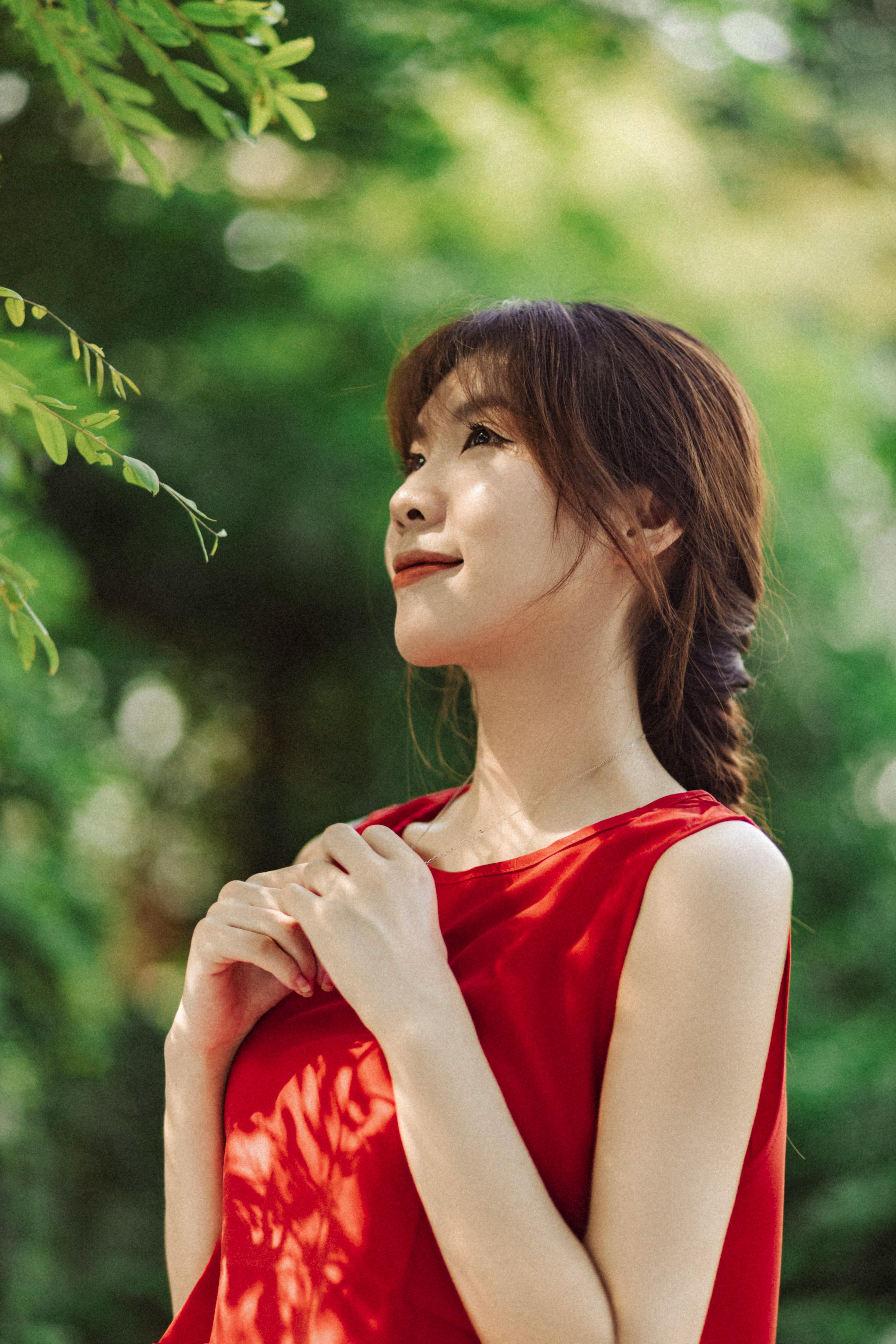 一幅宁静的肖像画，一位穿着红色连衣裙的女人被郁郁葱葱的绿叶包围着