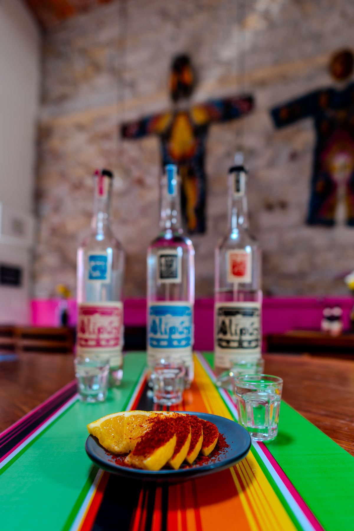 Colorful display of Alipus mezcal bottles with sliced lemons and vibrant tablecloth.