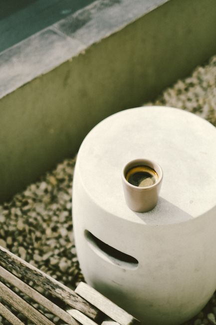 A single cup of coffee sits on a minimalist concrete table outdoors, capturing a tranquil morning vibe.
