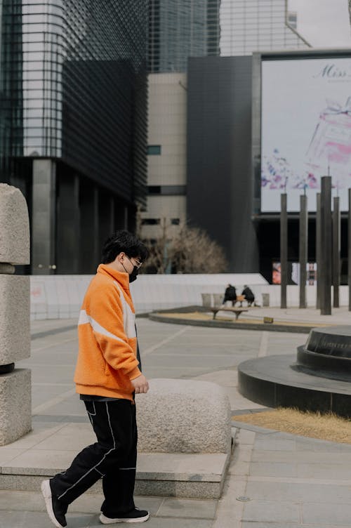 A person walking down a sidewalk in an orange jacket