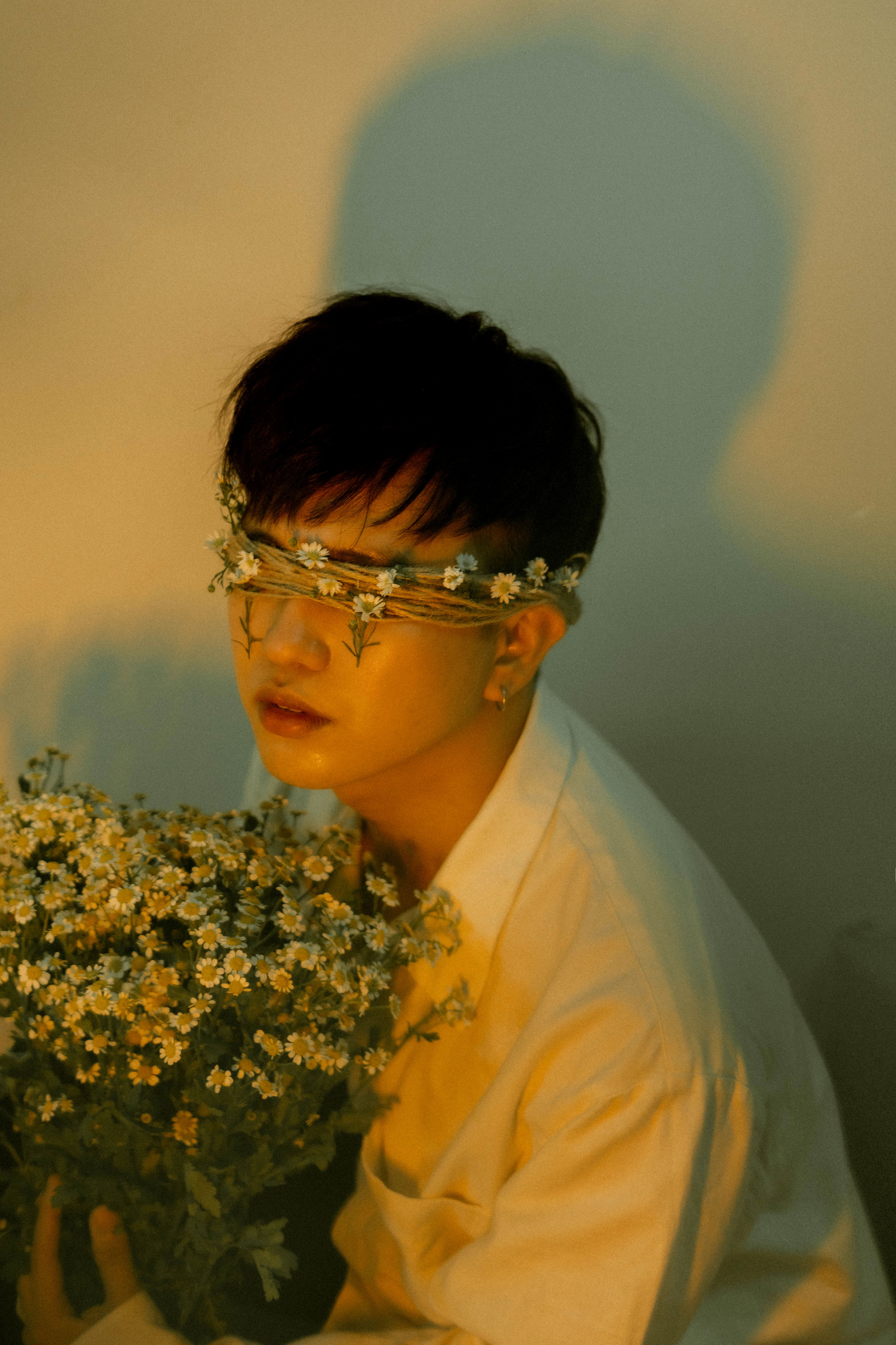 An artistic shot of a man with daisy chain blindfold holding a bouquet, evoking emotions.