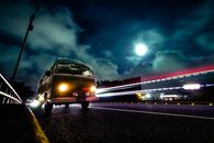 一辆老式大众货车在夜间高速公路上行驶，拥有引人注目的灯光轨迹和满月背景