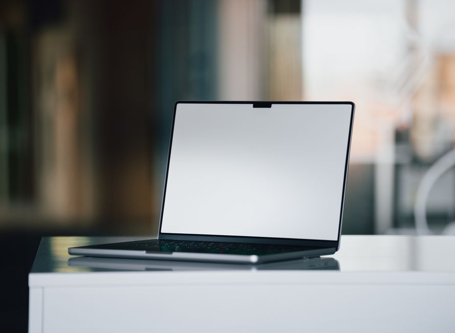 A sleek laptop with a blank screen sits on a white desk in a contemporary office setting.
