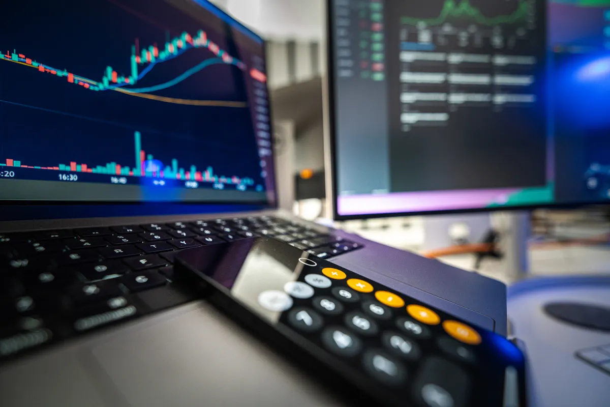 A laptop and desktop screen showing financial analysis alongside a calculator, the planning stage before committing to a webhook automation subscription.