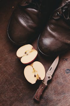 这幅经典的静物画以复古皮鞋、折叠刀和质朴表面上的苹果片为特色