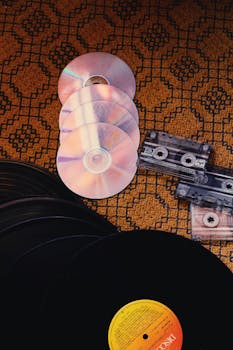A nostalgic collection of CDs, cassette tapes, and vinyl records on a patterned background.