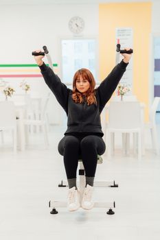Young woman lifting dumbbells during an indoor workout session, promoting fitness and health.