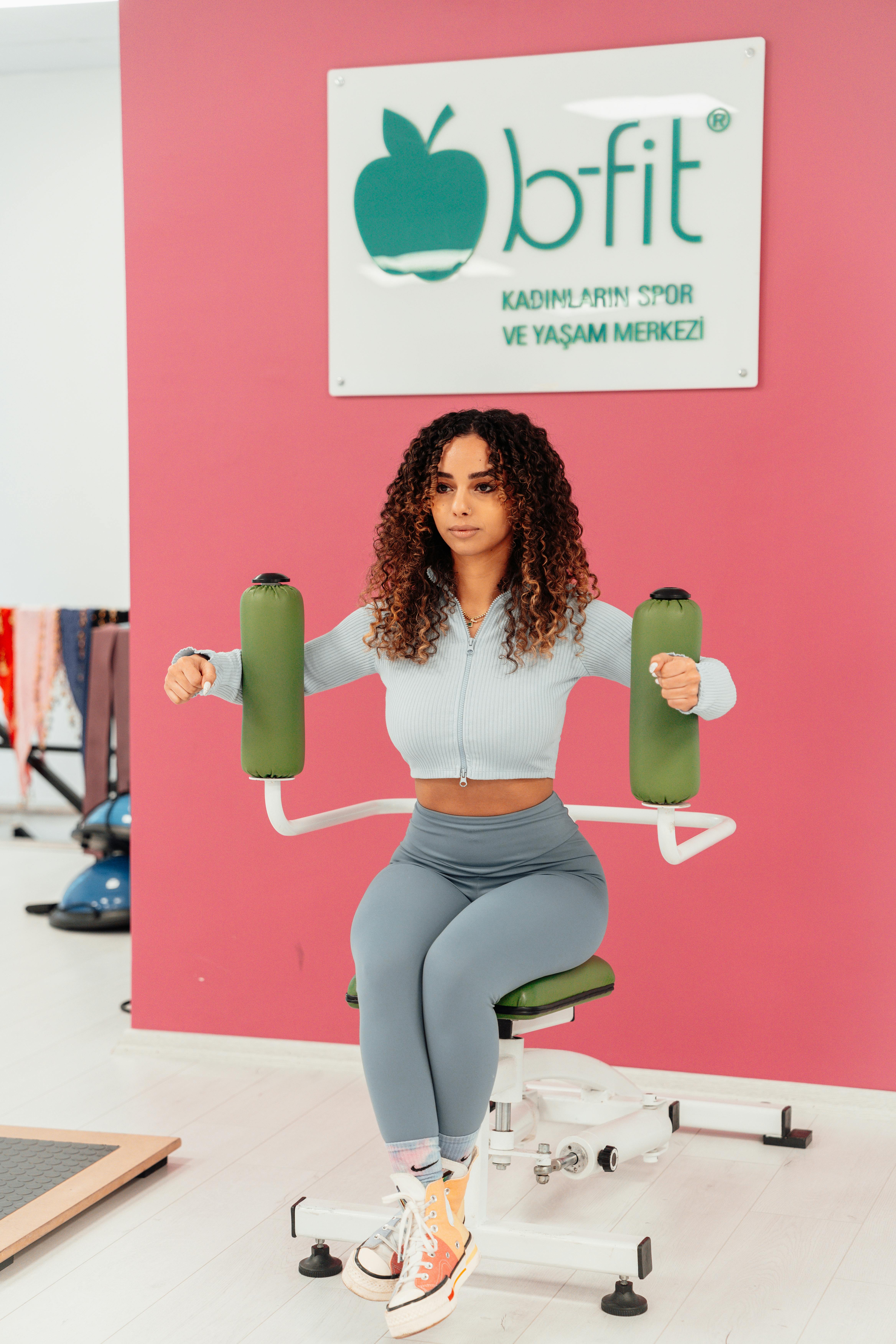 woman with curly hair exercising against pink wall