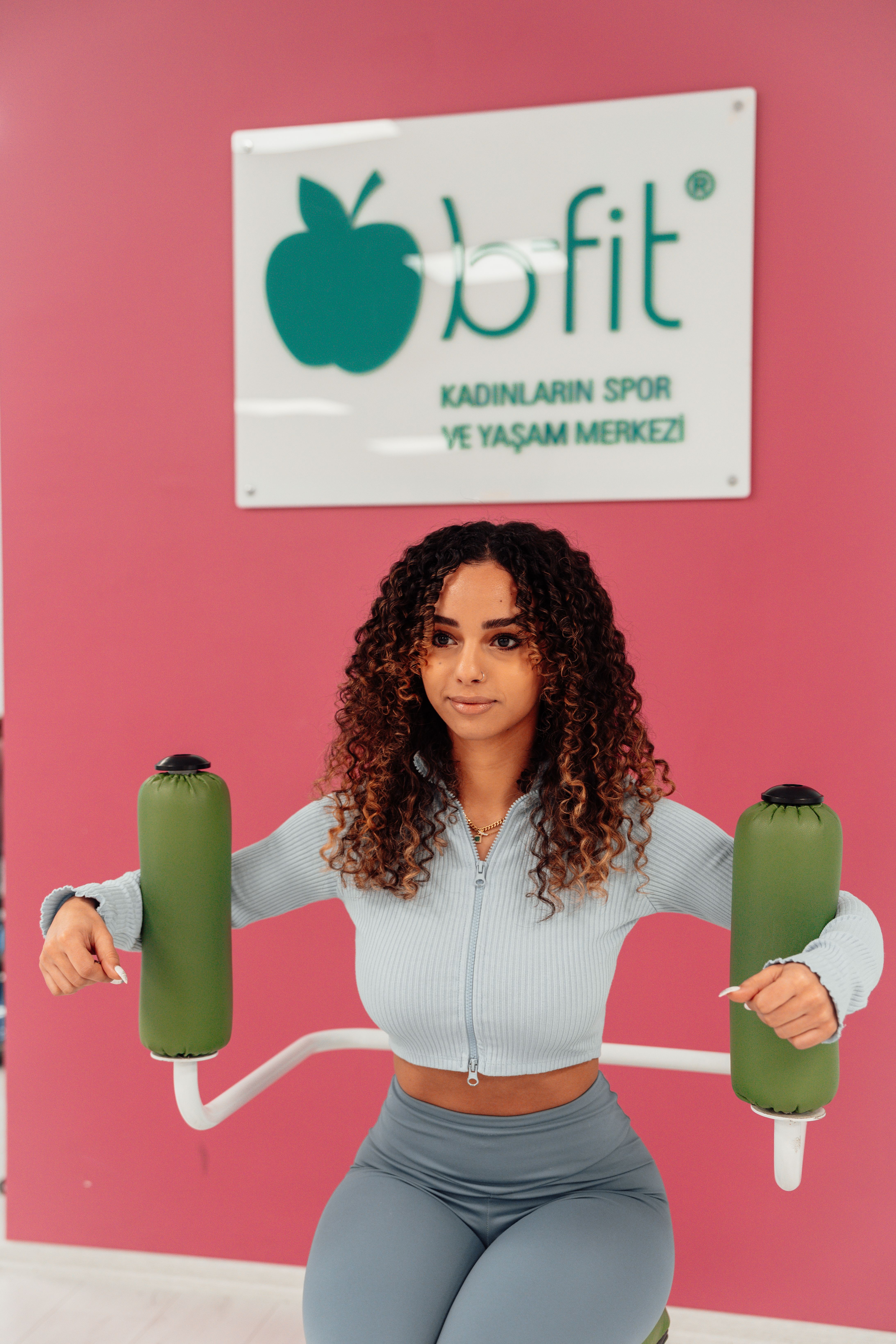 A young woman in a gym performing exercises against a vibrant pink wall in Yalova, Türkiye.