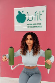 A young woman in a gym performing exercises against a vibrant pink wall in Yalova, Türkiye.