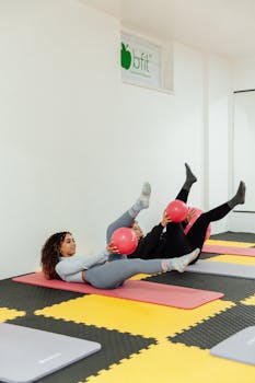 Two women engaging in a fitness routine with pink exercise balls at a modern gym.