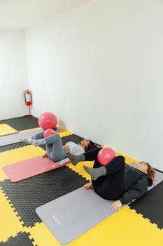 Two women working out with fitness balls on mats in a gym.