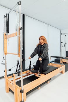 Woman practicing fitness exercises on a Pilates reformer in a gym setting.