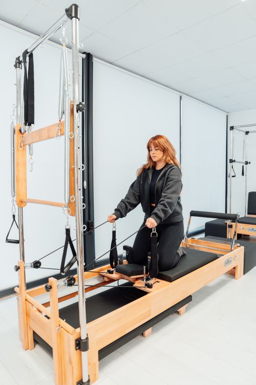 Free Woman practicing fitness exercises on a Pilates reformer in a gym setting. Stock Photo