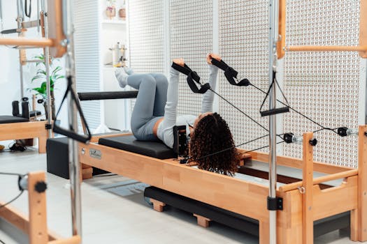 A woman practicing pilates on a reformer machine in a modern white studio setting.