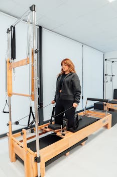 Woman practicing pilates on a tower reformer in a bright studio setting.