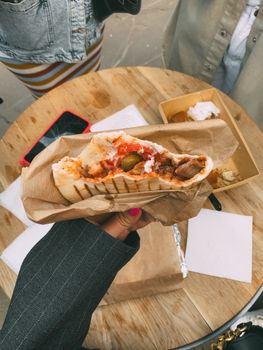 A person holds a delicious kebab wrap over a wooden table outdoors, showcasing vibrant street food culture.