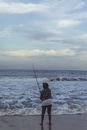 日落时分，一个人在海滩上静静垂钓，海浪轻柔，天空多云