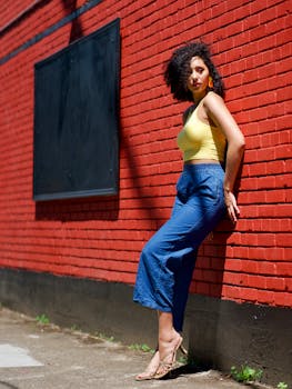 一位卷发优雅的女子倚在充满活力的红砖墙上，展现着夏季的时尚