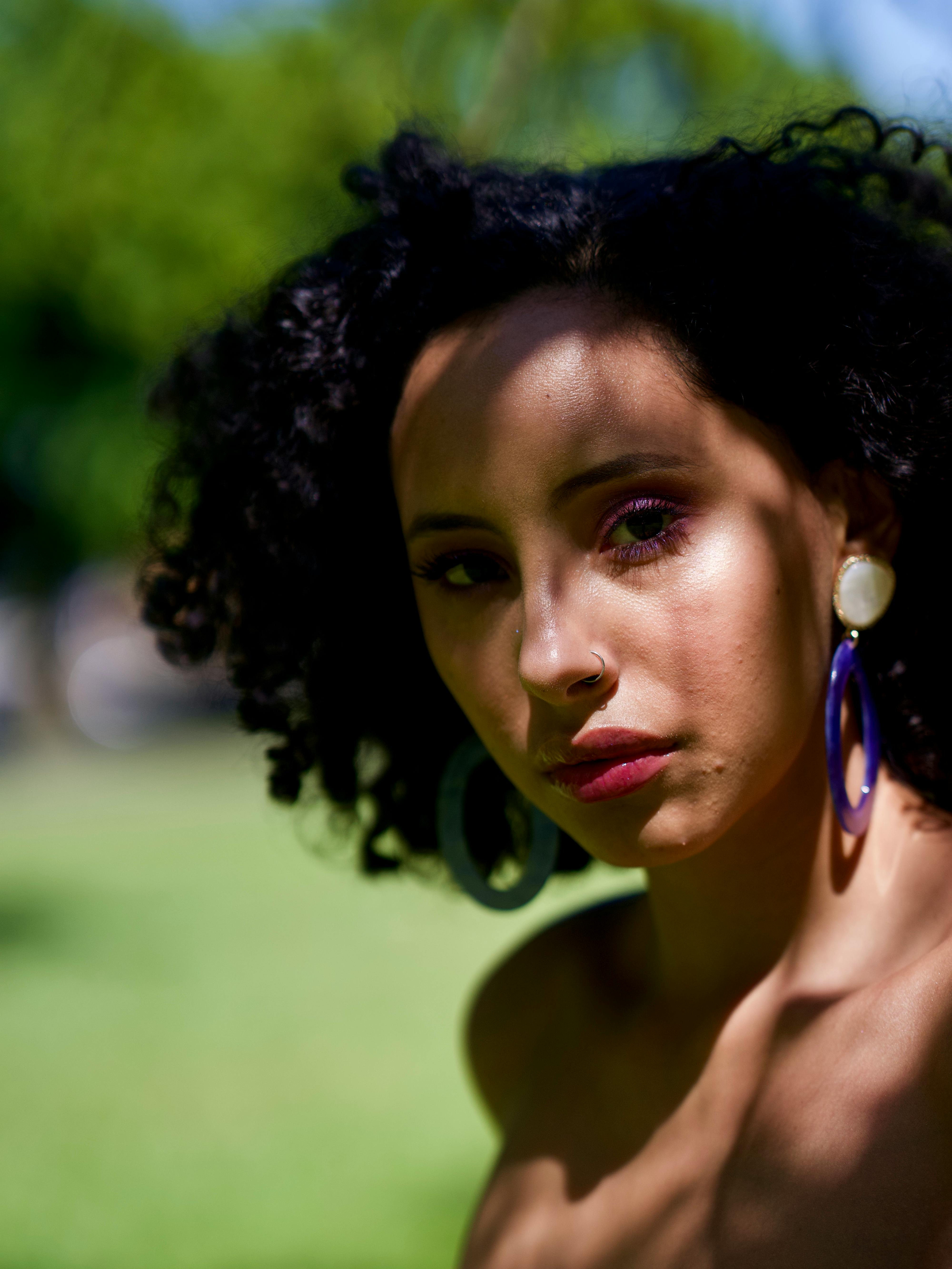 自然光线下，一位卷发、戴着精致耳环的女性在户外留下美丽的肖像