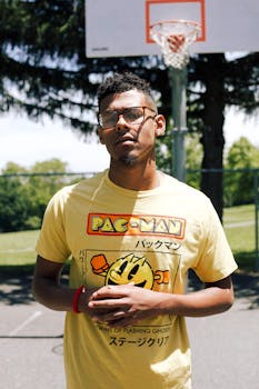 Adult man in a yellow t-shirt posing in front of a basketball hoop outdoors.