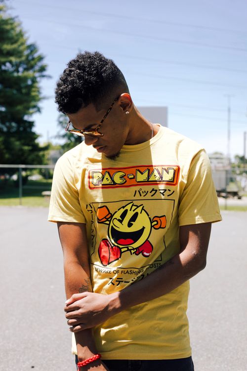 Free Casually dressed young man wearing a Pac-Man t-shirt, looking down outdoors under bright sunlight. Stock Photo