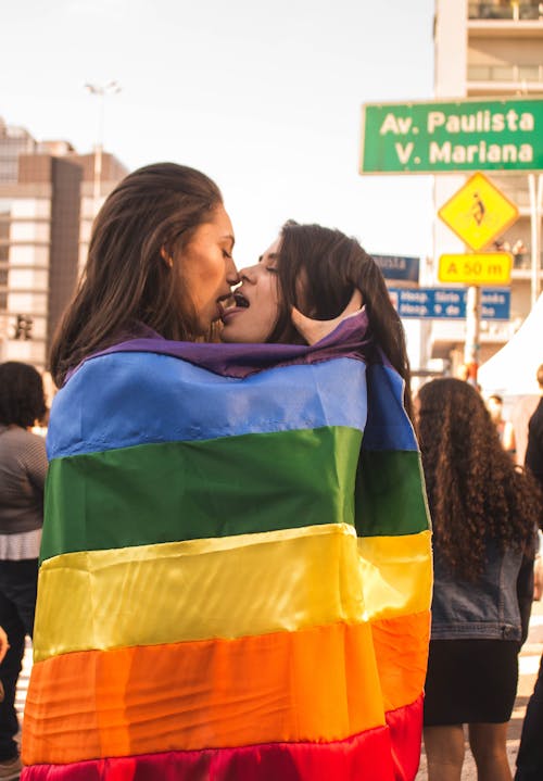 Two Women Kissing While Wrapped in Rainbow Flag
