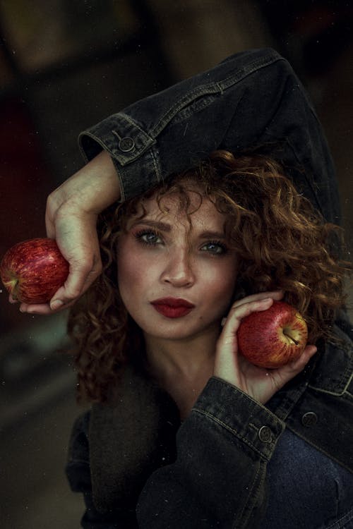 Photo of Woman Wearing Blue Denim Jacket Posing With Two Red Apple