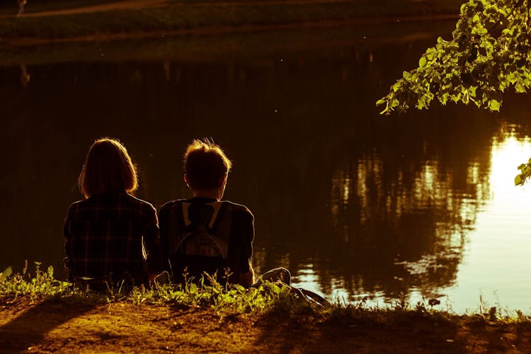 Woman And Man Sitting Beside Lake