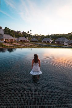 日落时分，一名身穿白色连衣裙的女子站在泰国度假村的无边泳池中