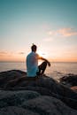 在泰国素叻他尼，一名男子坐在海边的岩石上，欣赏着色彩缤纷的日落