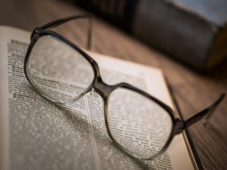 Close-up of a pair of eyeglasses resting on an open book, emphasizing reading and knowledge.