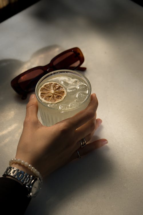 A person holding a drink with a lemon slice