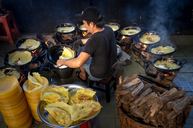 Man cooks multiple dishes on open flames, showcasing authentic street food preparation.