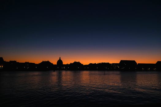 哥本哈根的天际线剪影，倒映在宁静的水面上，与充满活力的日落交相辉映