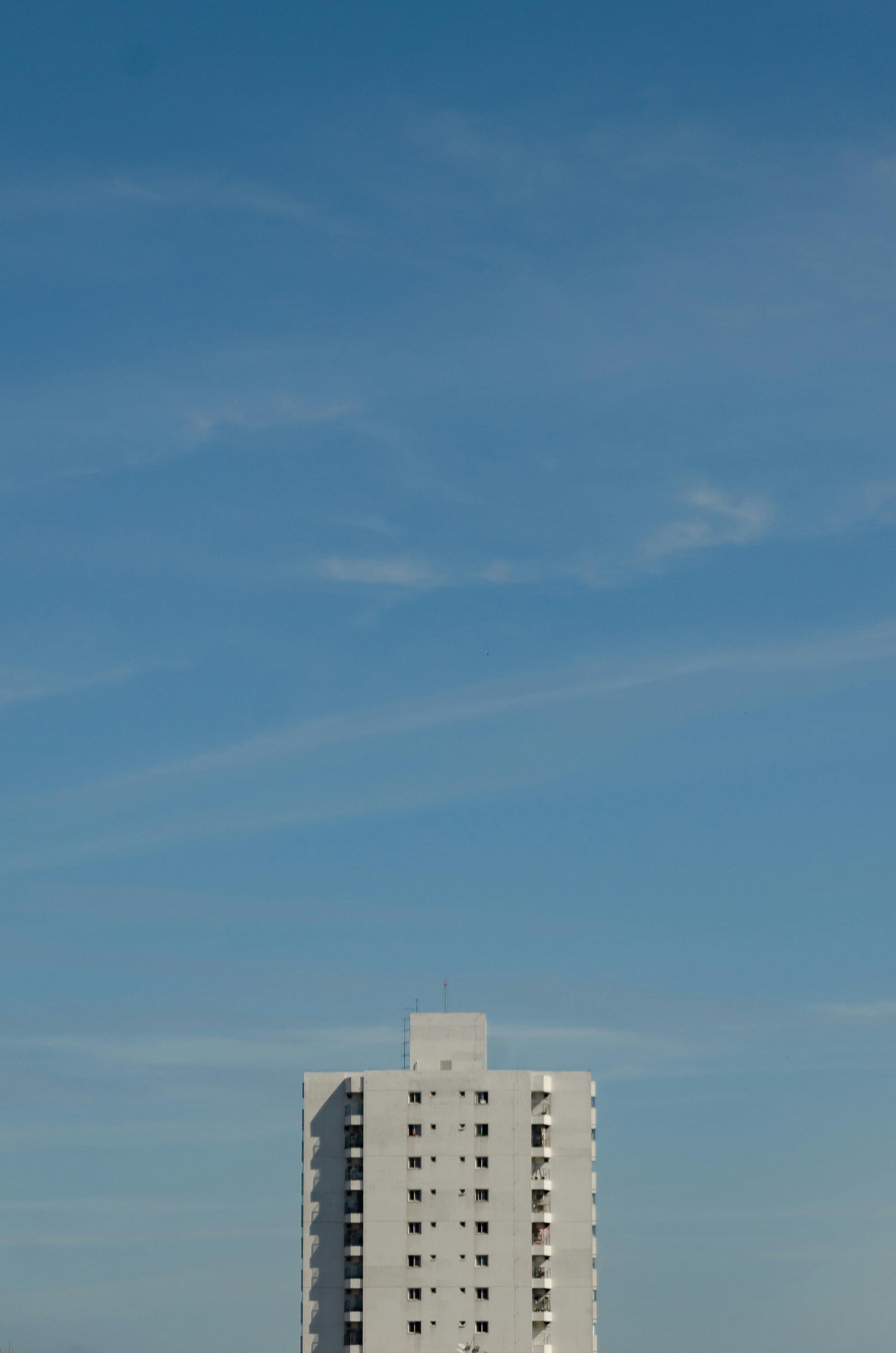 一座现代高层建筑孤独地矗立在清澈的蓝天下，展现了城市建筑的样貌