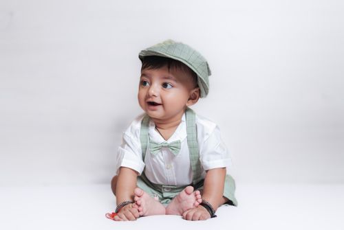 Free Charming studio portrait of a baby boy in a green outfit, sitting and smiling on a white background. Stock Photo